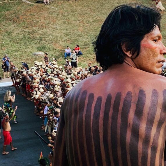 Un individu au premier plan regarde au loin, derrière lui une foule d'autochtones manifeste contre le président jair bolsonaro, à Brasilia au Brésil