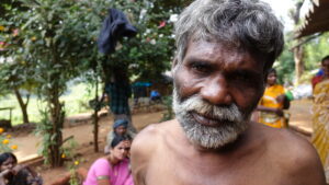 Homme Jenu Kuruba au premier plan. Derrière lui, des femmes Jenu Kuruba vêtues de tenues traditionnelles.