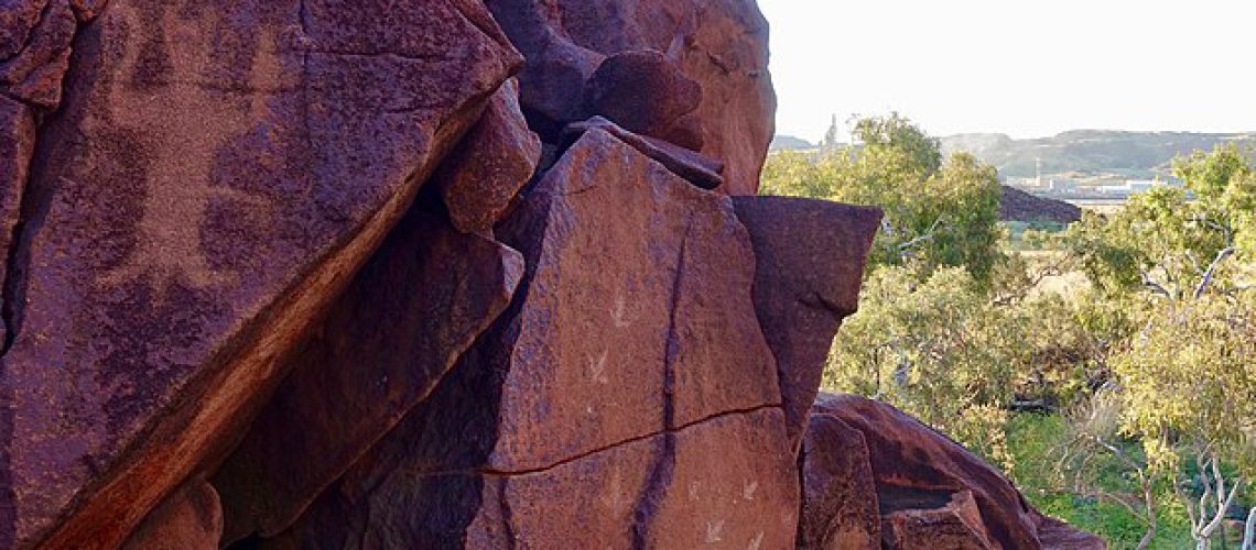 Sur les roches rouges de Murujuga, des gravures ancestrales. L'une d'elle semble avoir une forme humaine. En fond, la forêt aride australienne