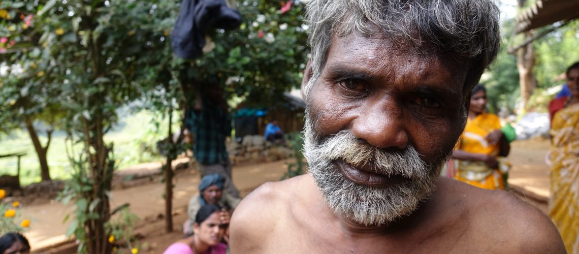 Homme Jenu Kuruba au premier plan. Derrière lui, des femmes Jenu Kuruba vêtues de tenues traditionnelles.